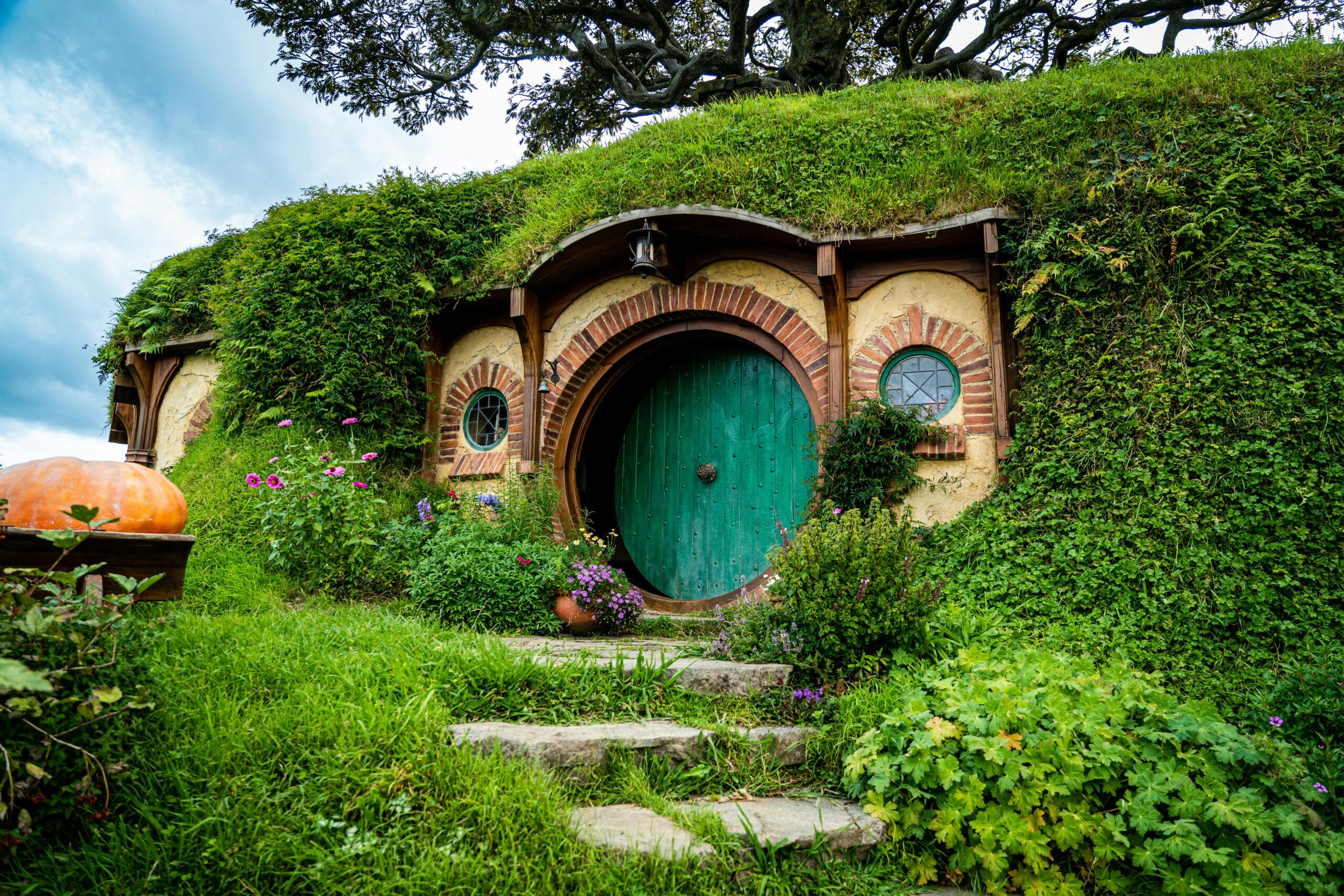 Picturesque Hobbiton house with a lush green roof and round door surrounded by vibrant garden.