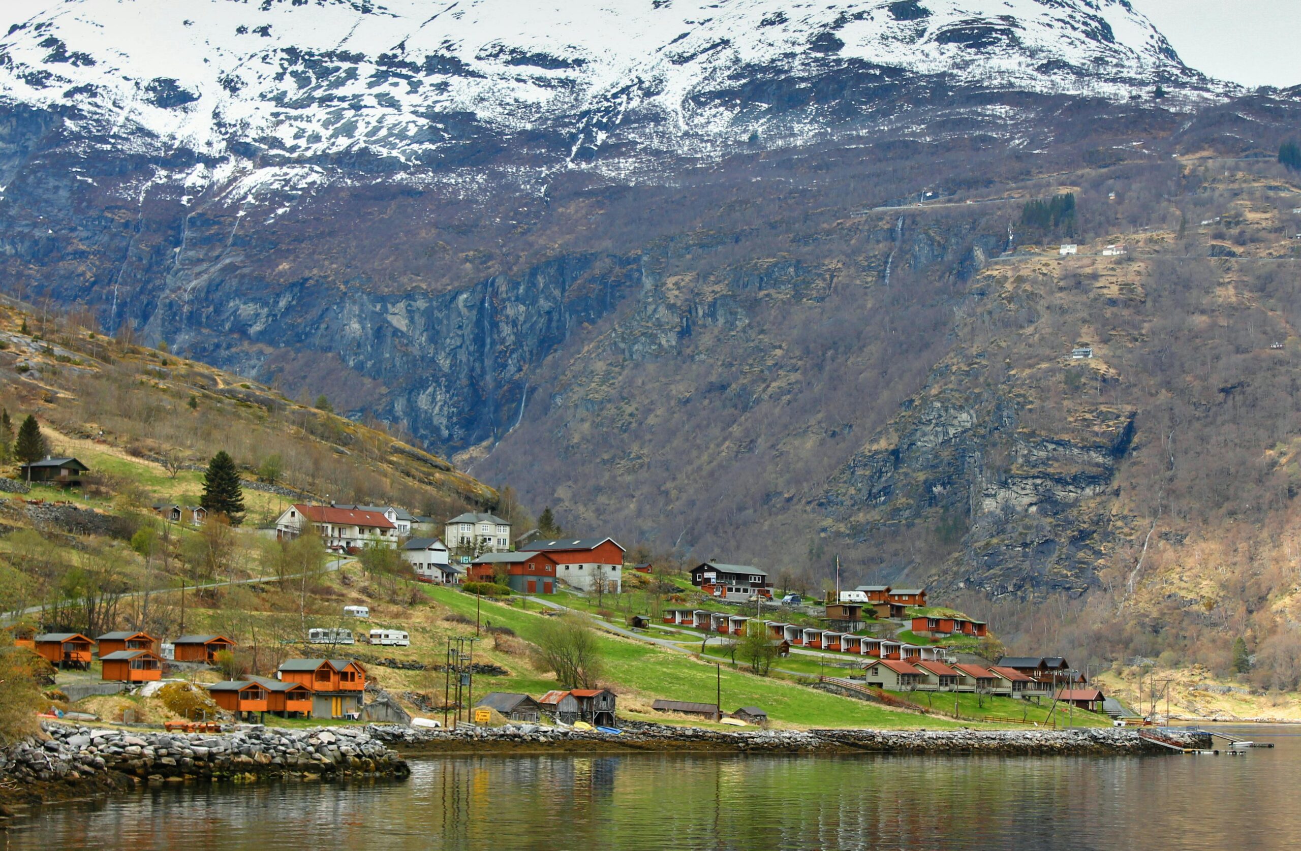 Picturesque village nestled in a Norwegian fjord, surrounded by snowy mountains and tranquil waters.